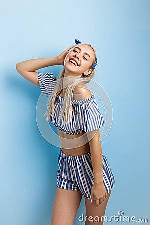 Joyful and excited beautiful blonde girl in summer outfit, posing at camera, standing over blue background Stock Photo