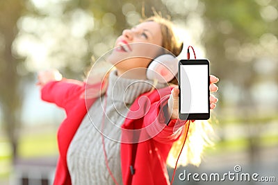 Joyful girl listening music and showing phone screen in winter Stock Photo