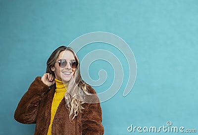 Joyful girl with long blond hair smiles. European girl in yellow sweater, faux fur coat and sunglasses. Autumn clothes Stock Photo