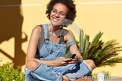 Joyful girl student listens audio book in earphones, has online courses, enjoys spending time in tropical place, keeps Stock Photo