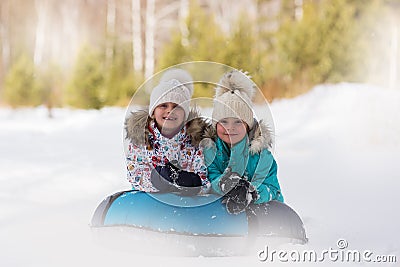 Joyful girls ride a tubing from a hill together. Winter holiday Stock Photo