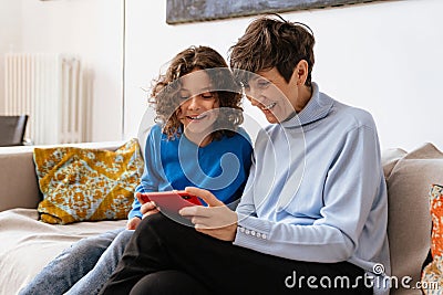 Joyful grandmother and grandson using smartphone together while sitting on sofa Stock Photo