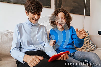 Joyful grandmother and grandson playing games on smartphone while sitting on sofa Stock Photo