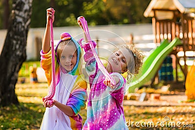 Joyful happy girls in rainbow costumes play slime. Girls walk in the park in uniforms. Children with slime Stock Photo