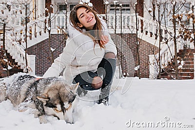Joyful happy young woman having fun with cute husky dog in snow on street. Cheerful mood, winter snowing time, waiting Stock Photo