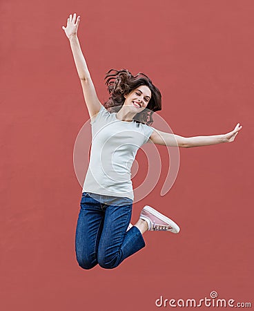 Joyful happy young woman jumping against red wall, beautiful girl enjoy life Stock Photo