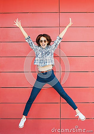 Joyful happy young woman jumping against red wall. Excited beautiful girl portrait Stock Photo