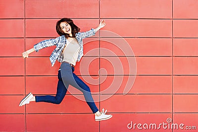 Joyful happy young woman jumping against red wall. Excited beautiful girl portrait Stock Photo