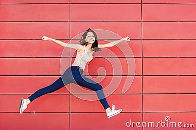 Joyful happy young woman jumping against red wall. Excited beautiful girl portrait Stock Photo