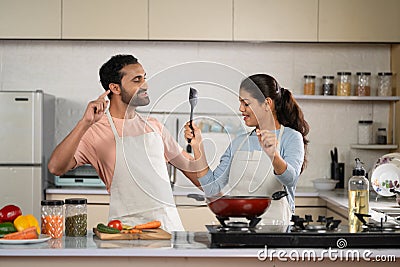 Joyful Indian couples at kitchen dancing together while cooking together during weekend holidays - concept of Stock Photo