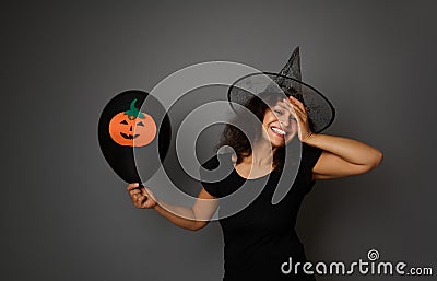 Joyful laughing woman in magic Halloween wizard hat looks at camera, holds black balloon with felt-cut pumpkin, smiles with Stock Photo