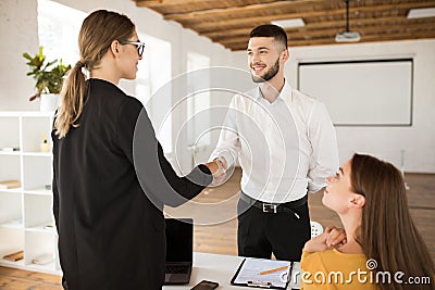 Joyful male applicant happily shaking employer hand. Young handsome man in shirt getting new job after interview in Stock Photo