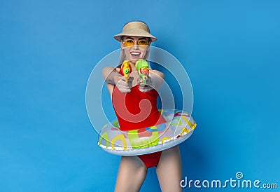Joyful Millennial Girl In Swimsuit Playfully Aiming With Water Guns At Camera Stock Photo