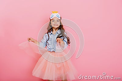 Joyful pretty young girl with long brunette hair dancing in tulle skirt isolated on pink background. Amazing cute little Stock Photo