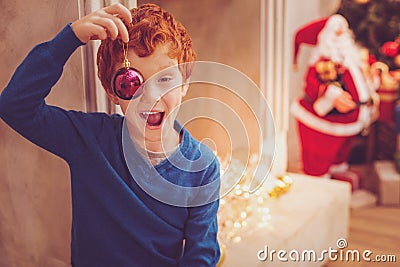 Joyful red-haired boy covering his eye with a Christmas bauble Stock Photo