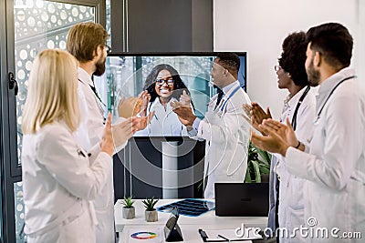 Joyful team of multiracial doctors during online video meeting indoors, clapping hands after successful presentation of Stock Photo