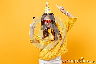 Joyful woman in orange funny glasses birthday party hat with playing pipe rising hands pointing index fingers up Stock Photo