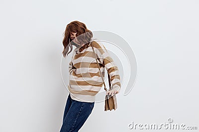 a joyful woman stands on a white background in a striped sweater and a bag on her shoulder , put her second hand on the Stock Photo