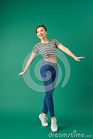 Joyful young Asian woman standing on one leg. Full length view of blissful girl dancing on green background Stock Photo