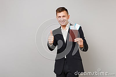 Joyful young business man in classic suit showing thumb up, holding passport, boarding pass ticket in hand isolated on Stock Photo
