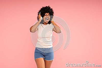 Joyful young woman with afro hairstyle dancing, listening music in headphones, having fun alone. Happy girl posing Stock Photo