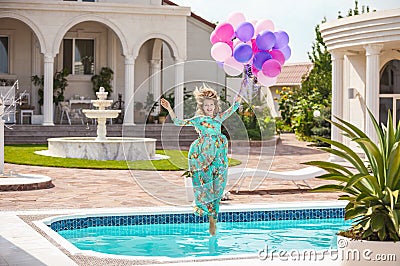 Joyful young woman jumping into the pool while holding a bunch of balloons Stock Photo