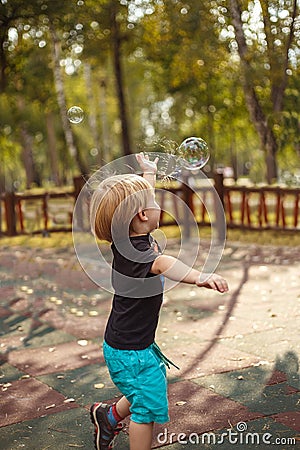 Joyfull little boy burst soapbubble in a jump with a hand Stock Photo