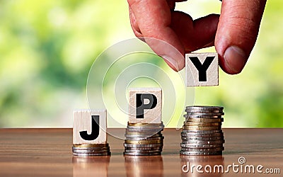 JPY Japan currency word symbol - business concept. Hands put wooden block on stacked increasing coin Stock Photo