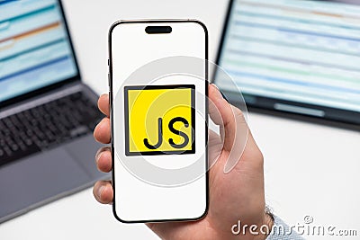 JS logo on the screen of smartphone in mans hand on the workplace background Editorial Stock Photo