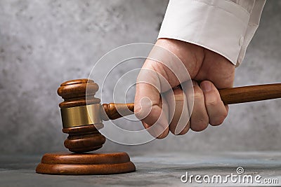 Judge gavel in hand against gray wall background, sentencing concept Stock Photo