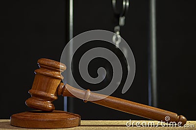 The judge`s wooden hammer for sentencing against the background of bars and handcuffs. Concept: court session, trial, sentencing. Stock Photo