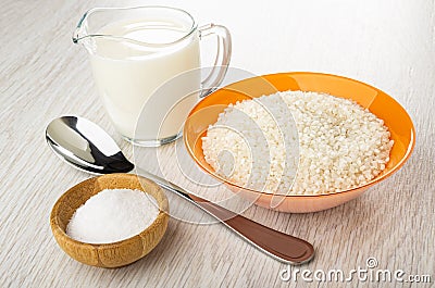 Jug of milk, bowl with raw rice, spoon, salt cellar on wooden table Stock Photo