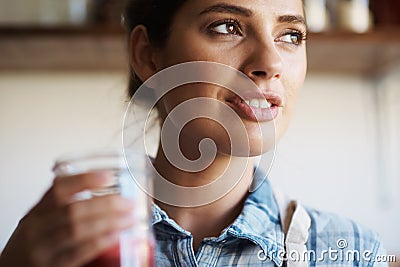The juice was definitely worth the squeeze. A beautiful young woman standing indoors and drinking freshly-juiced juice. Stock Photo