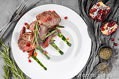 Juicy medium beef fillet steaks mignon with green beans, pomegranate and sauce in plate on grey background Stock Photo