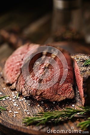 Juicy medium Beef Rib Eye steak slices on wooden board with herbs spices and salt Stock Photo