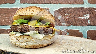 Juicy cheeseburger with chili pepper, tomato, lettuce and cucumber pickle on a natural wooden tray with vintage brick wall on back Stock Photo