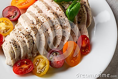 Juicy chicken fillet cooked under vacuum at low temperature. Sliced chicken breast and halves of fresh cherry tomatoes on a white Stock Photo