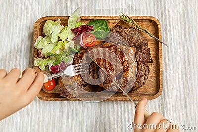 A juicy fresh roasting piece of steak on a wooden rectangular dish is decorated with fresh salad and cherry pardons. Stock Photo