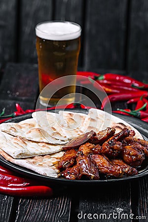 Juicy fried chicken wings glass of beer and chilli peppers on wood backiground Stock Photo