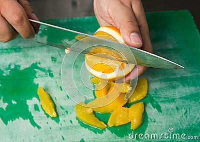 A juicy orange being sliced into segments on a green fruit and vegetable chopping board. organic fruit and vegetables Stock Photo