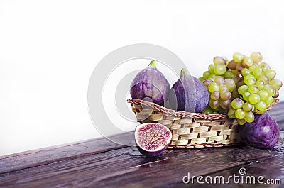 Juicy raisins and several ripe figs in a fruit basket on a white and dark wooden background. fresh fruits, natural vitamin Stock Photo