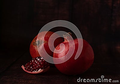 Juicy ripe pomegranates of dark red color on a dark background with a small piece of broken off pomegranate with fruit Stock Photo