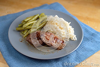 Juicy roasted lamb fillets with green beans and rice, the dish is served on a blue plate and napkin on a wooden table Stock Photo