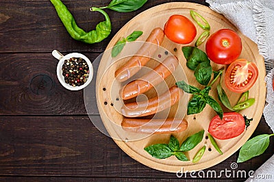 Juicy sausages with tomatoes and basil on a round cutting board on a dark wooden background Stock Photo