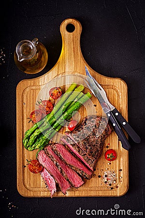 Juicy steak rare beef with spices on a wooden board and garnish of asparagus. Stock Photo