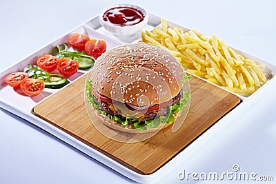 Juicy tasty hamburger on a wooden cutting board with french fried fries, vegetables and ketchup. Isolated composition on Stock Photo