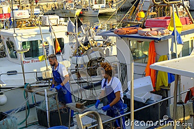 July 2022 Senigallia, Italy: Two sailors working on ship in the harbour across other boats. Editorial Stock Photo