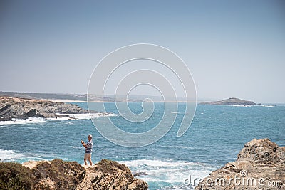 Porto Covo, Portugal - an unidentified man takes a selfie on top of a cliff of the praia dos Buizinhos beach Editorial Stock Photo