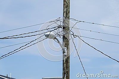 Jumble of wires connecting to the top of a wooden telephone utility pole with a street light attached to it Stock Photo