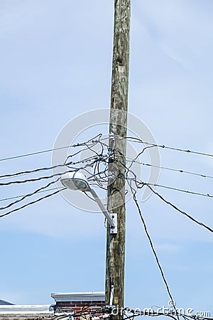 Jumble of wires connecting to the top of a wooden telephone utility pole with a street light attached to it Stock Photo